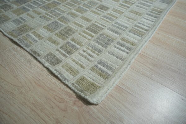 Cream rug with a textured, raised geometric pattern in gray and pale tan on light wood planks.