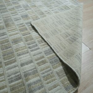 Close-up of a low-pile rug with beige, gray, and cream rectangular patterns on light wood flooring.
