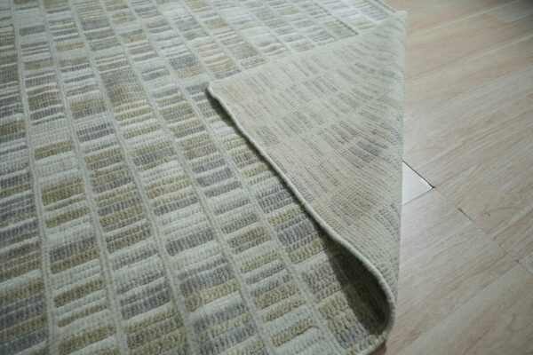Close-up of a low-pile rug with beige, gray, and cream rectangular patterns on light wood flooring.