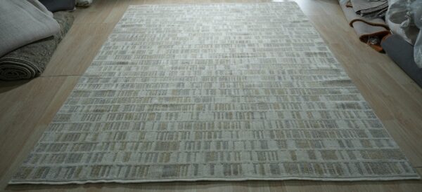 Neutral area rug with a repeating pattern of short gray and beige dashes on light wood flooring.