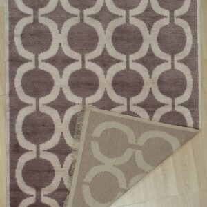 A mauve and beige geometric pattern rug with a folded corner rests on light wood flooring.