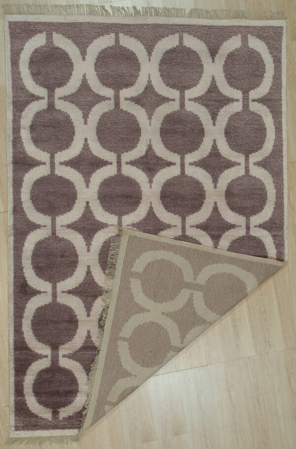 A mauve and beige geometric pattern rug with a folded corner rests on light wood flooring.