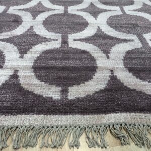 High-pile rug with dark taupe interlocking geometric circles and light fringes on a wooden floor.