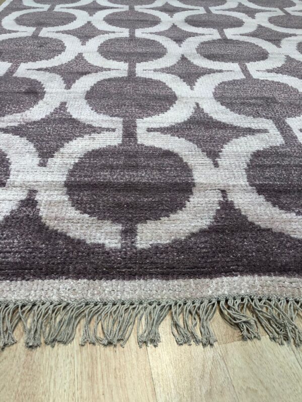 High-pile rug with dark taupe interlocking geometric circles and light fringes on a wooden floor.