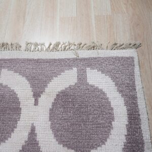 Geometric purple and cream rug with a short fringe and textured pile shown against light wood floor.