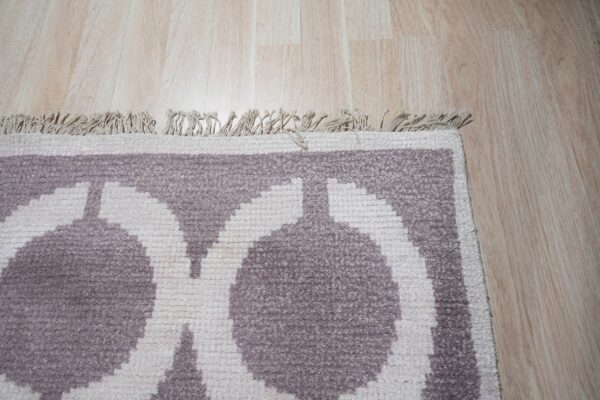Geometric purple and cream rug with a short fringe and textured pile shown against light wood floor.