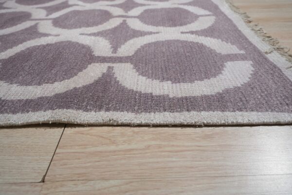 Low pile rug in taupe and ivory with a quatrefoil pattern shown on light wood flooring.