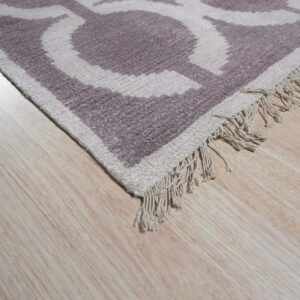 High-texture rug corner featuring a mauve and cream geometric pattern and short fringe on light wood flooring.