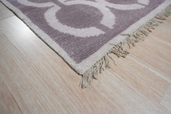 High-texture rug corner featuring a mauve and cream geometric pattern and short fringe on light wood flooring.
