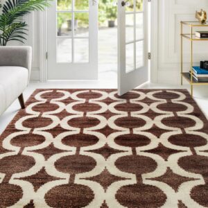 Brown and cream geometric area rug lies in a bright room with white furniture and open French doors.