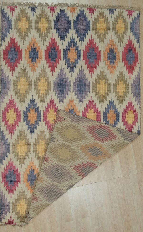 Multi-colored low-pile rug with repeated geometric diamond patterns folded over on pale hardwood floor.