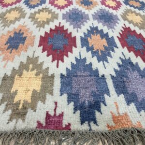 High pile rug with multicolor geometric patterns and gray fringe lies on light wood plank flooring.