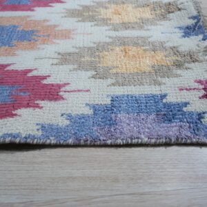 High-pile rug with geometric blue, pink, tan, and cream shapes lying on pale wood flooring.