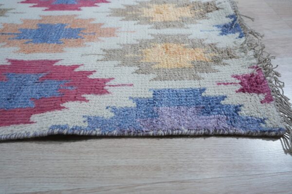 High-pile rug with geometric blue, pink, tan, and cream shapes lying on pale wood flooring.