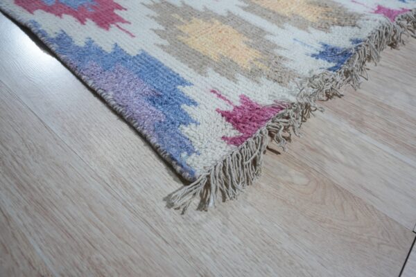 Medium pile rug with colorful ikat-style patterns and fringe rests on light wood-look flooring.