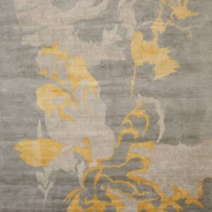 A low-pile gray rug with carved abstract patterns in light beige and golden yellow motifs.
