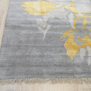 Gray medium-pile rug with yellow abstract patterns and fringe rests on light blonde wood flooring.