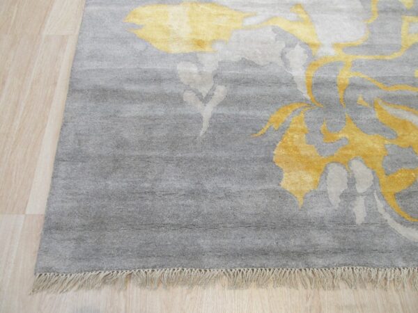 Gray medium-pile rug with yellow abstract patterns and fringe rests on light blonde wood flooring.