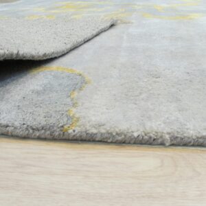 The plush gray rug with a yellow abstract pattern is rolled back on light wood flooring.