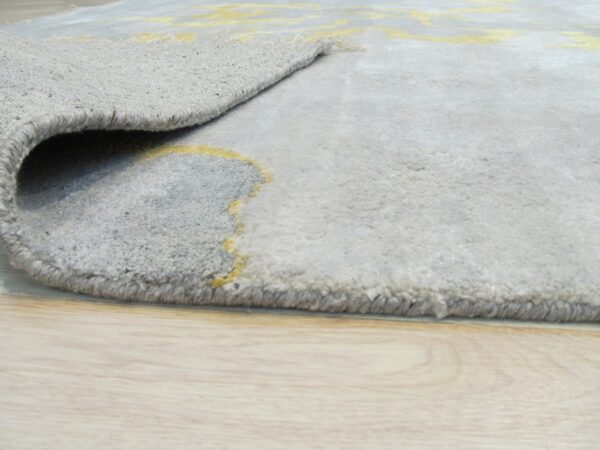 The plush gray rug with a yellow abstract pattern is rolled back on light wood flooring.