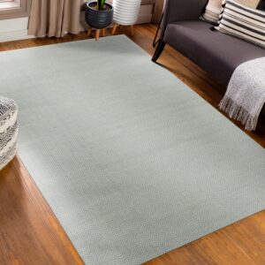 A light gray flatweave rug with a tight chevron pattern sits on a hardwood floor next to a dark sofa.