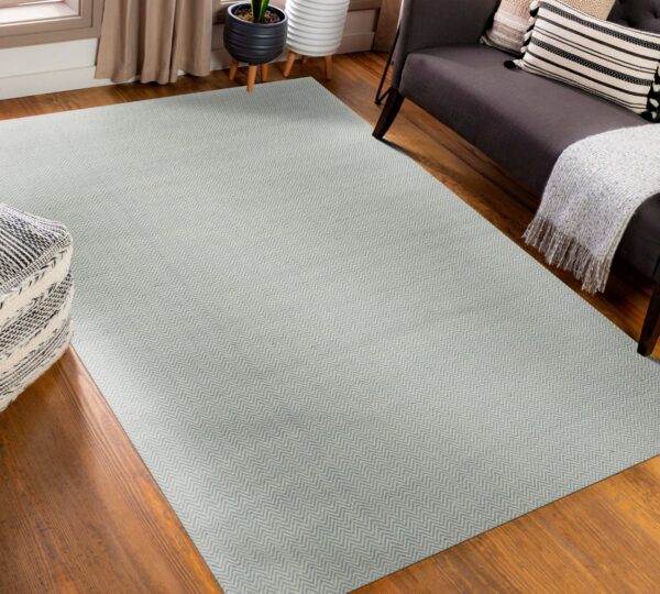 A light gray flatweave rug with a tight chevron pattern sits on a hardwood floor next to a dark sofa.