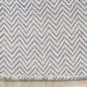 Close view of a blue and cream chevron flat weave rug edge on pale wood flooring.