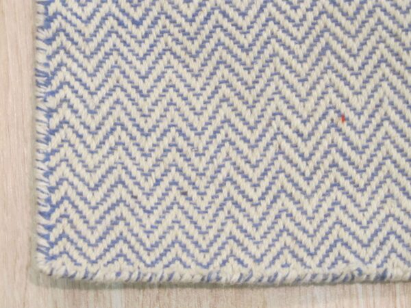 Close view of a blue and cream chevron flat weave rug edge on pale wood flooring.
