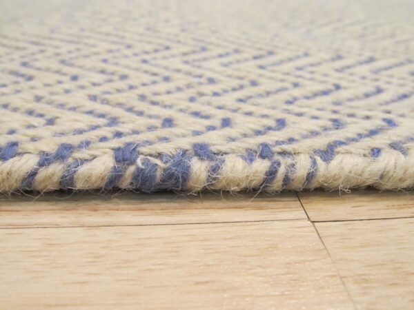Chunky, textured cream and blue chevron rug edge rests on light plank flooring.