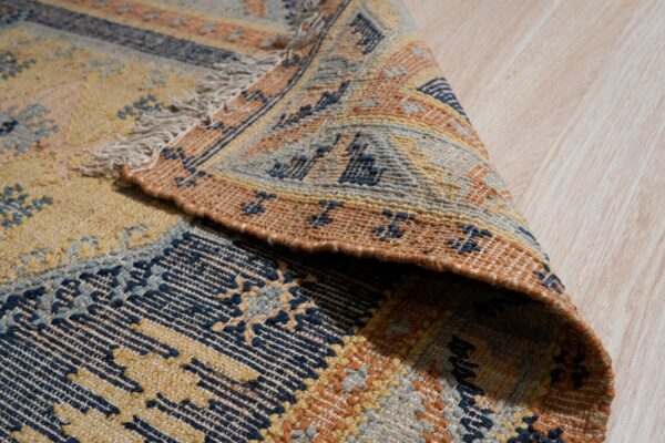 Low-pile rug with geometric patterns in navy, yellow, and orange folded on light wood flooring.