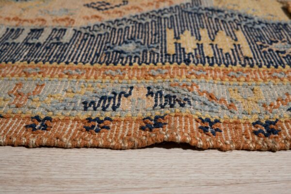 Woven rug detail showing navy, yellow, rust, and blue patterned bands resting on light wood flooring.
