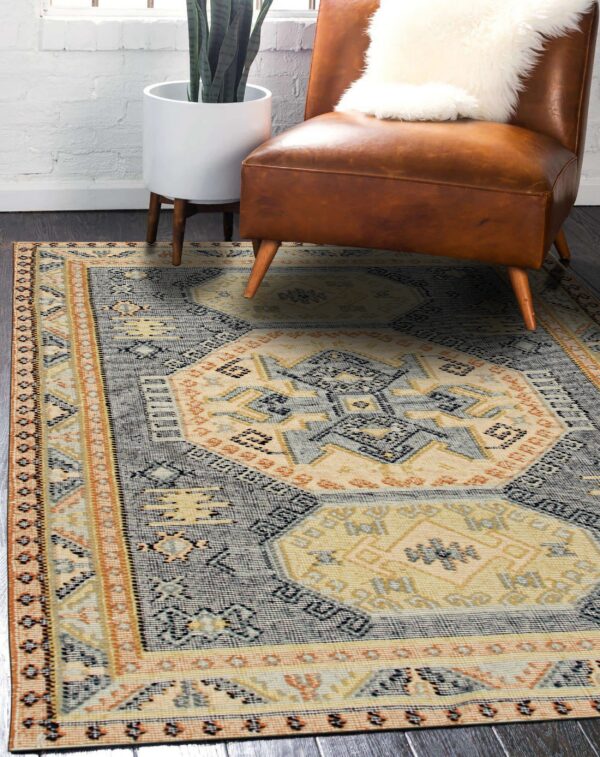 A low-pile rug featuring gray, cream, and orange geometric patterns sits beneath a brown leather chair.