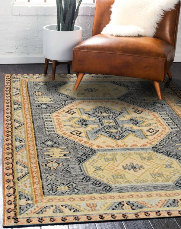 Gray and cream geometric rug with orange accents anchors a leather armchair on dark wood flooring.