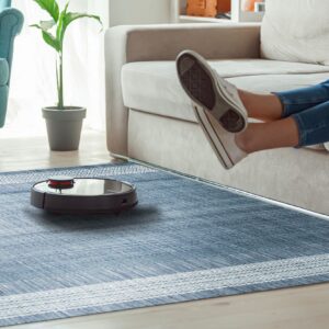 Textured blue area rug with white geometric borders sits on wood flooring near a beige sofa.