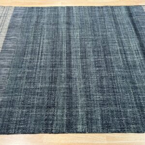 Textured blue flatweave rug with dark stripes and wide light borders featuring a diamond pattern on a wood floor.