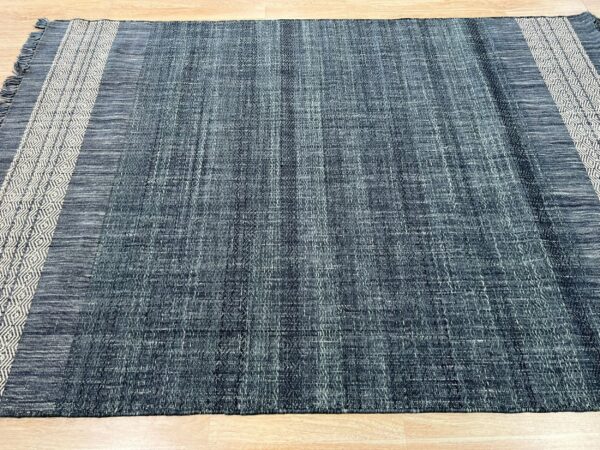 Textured blue flatweave rug with dark stripes and wide light borders featuring a diamond pattern on a wood floor.