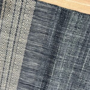 Low-pile navy rug with a vertical off-white geometric diamond stripe lying on light wood planks.