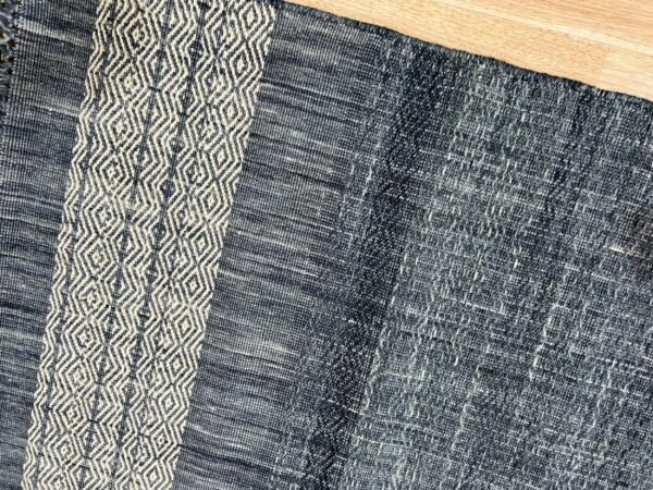 Low-pile navy rug with a vertical off-white geometric diamond stripe lying on light wood planks.