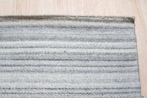 Low-pile rug with alternating heather gray and light gray horizontal stripes on a wood floor.