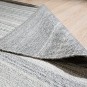 The edge of a gray and white striped flatweave rug is folded over a light wood floor.