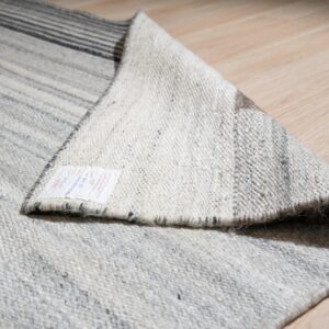 A gray and white striped rug folded over on light wood flooring, revealing a product tag and woven backing.