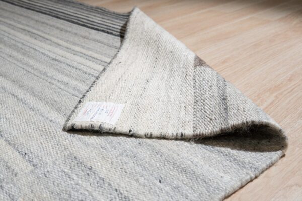 A gray and white striped rug folded over on light wood flooring, revealing a product tag and woven backing.