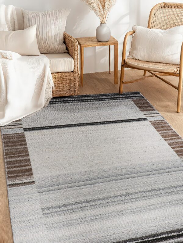 A light gray flatweave rug with charcoal and brown stripes on wood flooring beside wicker furniture.