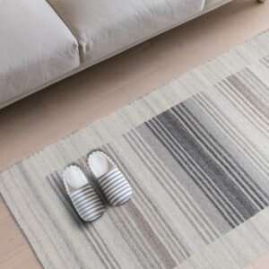 Flat-weave rug with gray and taupe stripes sits under a beige sofa on light wood flooring.