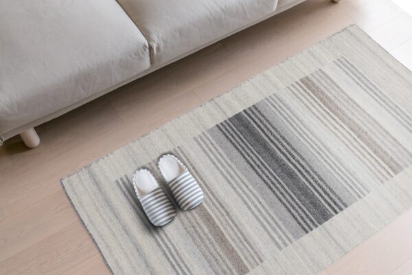 Flat-weave rug with gray and taupe stripes sits under a beige sofa on light wood flooring.