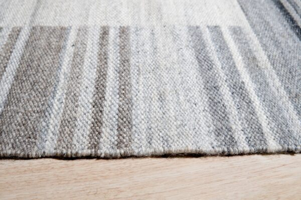 Close-up of a low-pile gray and white striped rug texture resting on light blonde wood flooring.