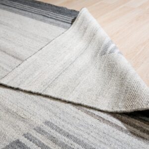Close-up of a gray and white striped rug, showing its woven texture, folded over light wood planks.
