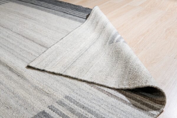 Close-up of a gray and white striped rug, showing its woven texture, folded over light wood planks.