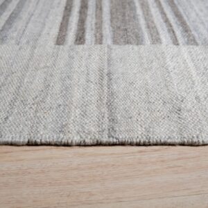 Close-up of the textured light gray rug edge resting on natural blonde wood plank flooring.