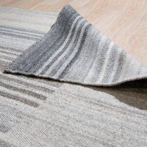 A gray and cream striped flatweave rug is partially folded back on a light wood floor.